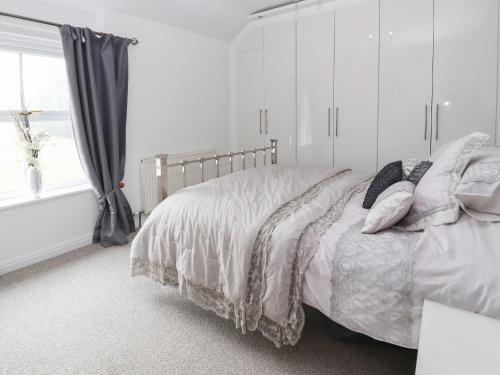 a white bedroom with a bed with pillows and a window at Park View Cottage in Mold