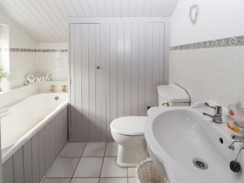 a white bathroom with a toilet and a tub and a sink at Park View Cottage in Mold