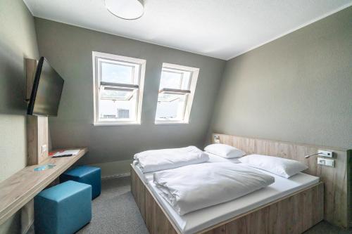 a bedroom with a bed with white sheets and two windows at WIROtel Warnemünde in Warnemünde