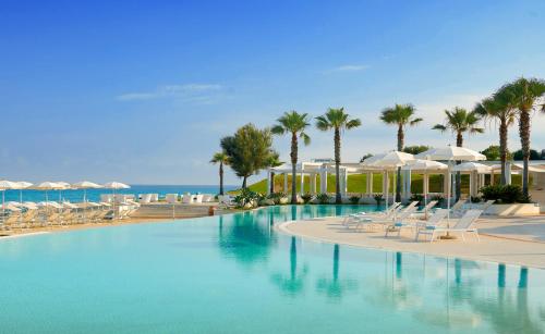 a swimming pool with chairs and umbrellas and the ocean at Capovaticano Resort Thalasso Spa in Capo Vaticano