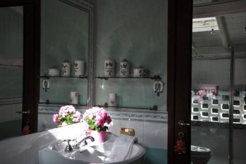 ein Badezimmer mit einem Waschbecken, einem Spiegel und Blumen in der Unterkunft la casa rossa nel bosco in Cantù