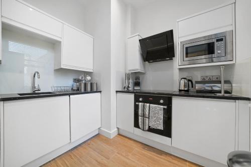 a kitchen with white cabinets and a microwave at City Prime Apartments in London