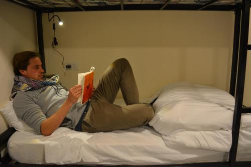 mężczyzna leżący na łóżku czytający książkę w obiekcie MOUNT41 Hostel w mieście Jerycho