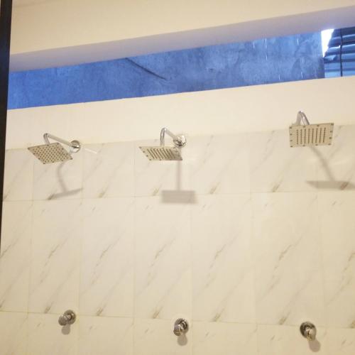 a shower with three shower heads on a white marble wall at Mega Hostel in Mirissa