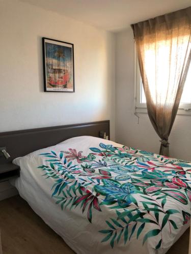 a bed with a colorful blanket on it with a window at Le Boucanier in Vieux-Boucau-les-Bains