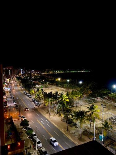 a city street with cars and palm trees at night at Praia Hotel Enseada in Maceió