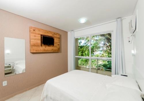 a bedroom with a white bed and a window at Pousada Castellammare in Bombinhas