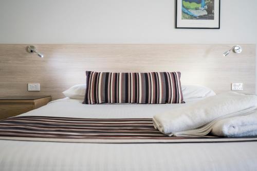 a bed with a striped pillow and two pillows on it at Avoca Beach Hotel in Avoca Beach