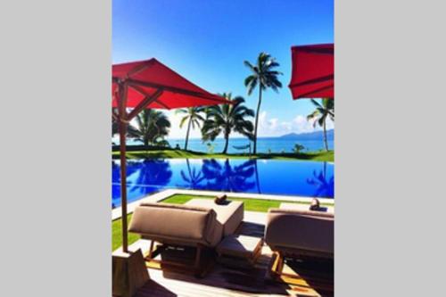 a patio with two chairs and a pool with palm trees at Villa Takali - CFC Certified in Pacific Harbour