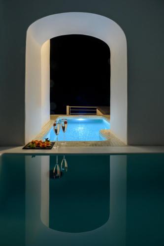 a pool with a table with a plate of food and glasses at Nefeles Luxury Suites in Fira