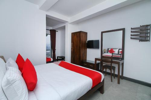 a bedroom with a bed with red pillows and a desk at Delphin Hotel in Nuwara Eliya