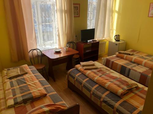 a room with three beds and a small table and a television at Hotel Sabina in Riga