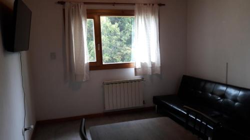 sala de estar con sofá de cuero negro y ventana en Departamento Victoria Bariloche en San Carlos de Bariloche