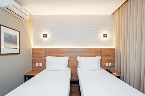 two beds in a hotel room with white sheets at Slaviero Curitiba Aeroporto in São José dos Pinhais