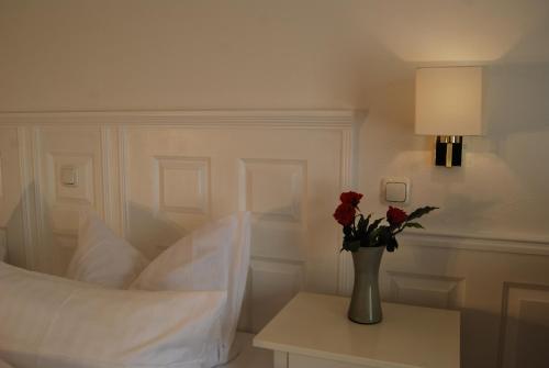 a white bedroom with a vase with roses on a table at Wohlfühlhotel Hörn van Diek Garni mit Schwimmbad in Bensersiel