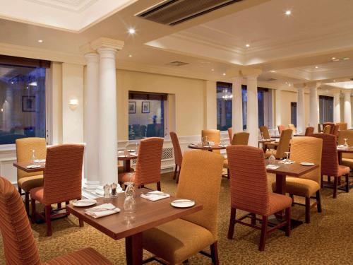 um restaurante com mesas e cadeiras de madeira e janelas em Mercure Winchester Wessex Hotel em Winchester