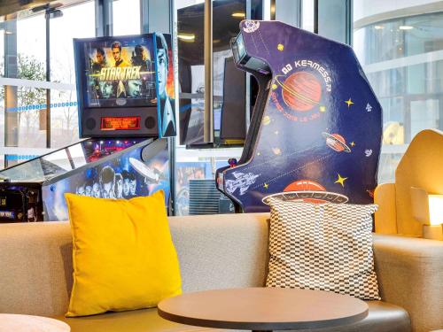 a couch with a pillow and a pinball machine at ibis Styles Paris Charles de Gaulle Airport in Roissy-en-France