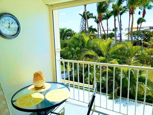 a balcony with a table and a clock and palm trees at studio hibiscus in Saint-François