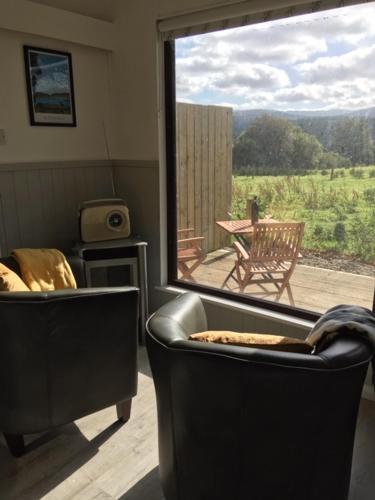 a living room with two chairs and a large window at Ade's River Cabin in Lettermacaward