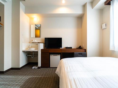 a hotel room with a bed and a desk with a television at Bande Hotel Tenpozan Higashi in Osaka