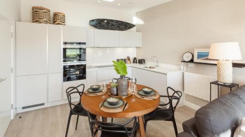 a kitchen and living room with a wooden table and chairs at 2 Woolacombe West - Luxury Apartment at Byron Woolacombe, only 4 minute walk to Woolacombe Beach! in Woolacombe