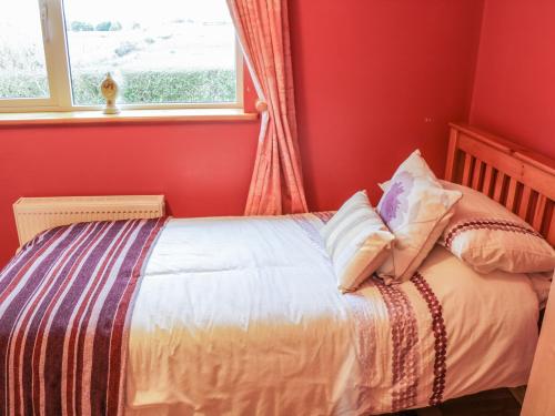 a bedroom with a bed with red walls and a window at Ellen's Cottage in Mountcharles