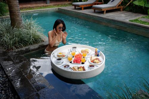 a woman sitting in a pool with a table in the water at Bumbak Park Villas in Canggu