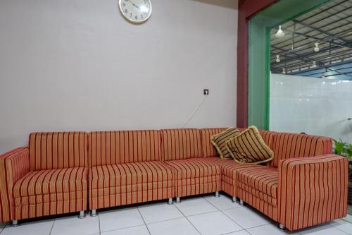 a red couch in a room with a clock on the wall at RedDoorz Syariah @ Hotel Wisma Indonesia Kendari in Kendari