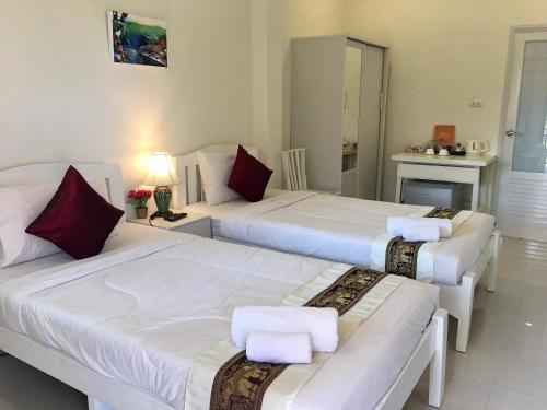 a bedroom with three beds with white sheets and red pillows at Naraya Homestay in San Pa Tong