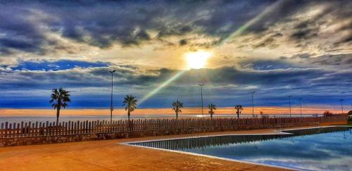 a sunset over a swimming pool with a rainbow in the sky at TAIGA Delta de l'Ebre in L'Ampolla