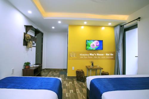 Cette chambre comprend 2 lits et une télévision sur un mur jaune. dans l'établissement May's House Hoi An, à Hội An