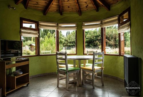 a dining room with a table and chairs and windows at Cabaña Piedemonte in Lago Puelo