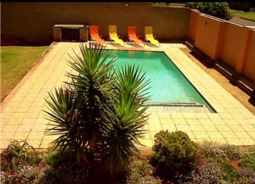 una piscina con sillas y palmeras. en SunSet West Self Catering Maraisburg Roodepoort en Johannesburgo