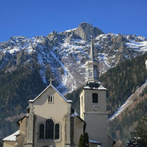 a church with a clock tower in front of a mountain at Hotel Le Chamonix in Chamonix-Mont-Blanc