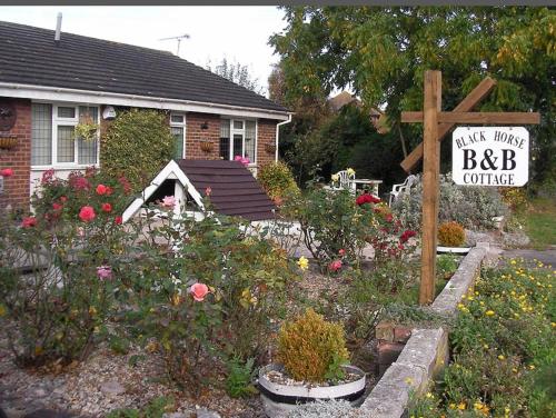 a house with a garden with flowers and a sign at Black horse cottage in Stonewood