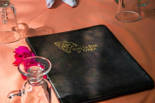 a table with a black book and a bottle and a flower at Hotel La Rosa de America in Alajuela City