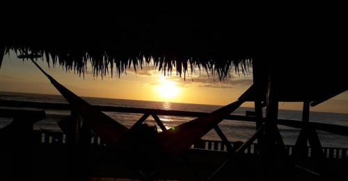 a sunset on the beach with a straw umbrella at Hostal Mirada al Mar in Las Tunas