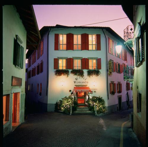 a white building with red shutters on a street at Hotel Romanda in Levico Terme