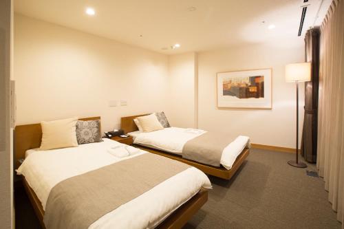 a hotel room with two beds and a lamp at 3 Wellness in Okayama