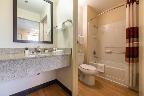 y baño con lavabo, aseo y espejo. en California Inn and Suites, Rancho Cordova, en Rancho Cordova