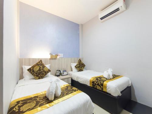 two beds in a room with white and yellow sheets at Top Garden Hotel in Hutan Melintang