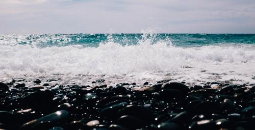 a rocky beach with a wave crashing on the ocean at Sui Tetti, Caressa de mä in Bordighera