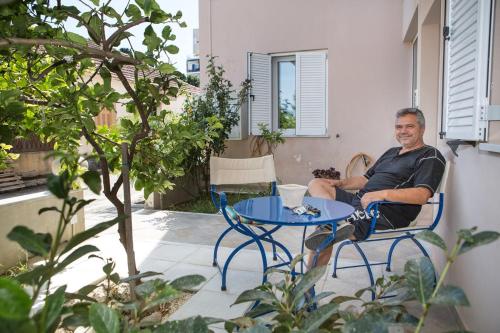 a man sitting in a chair next to a table at Manolatos Apartment Kefalonia in Lixouri