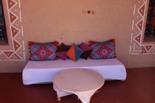 un letto con cuscini colorati e un tavolo in una stanza di Dar Timitar a El Kelaa des Mgouna
