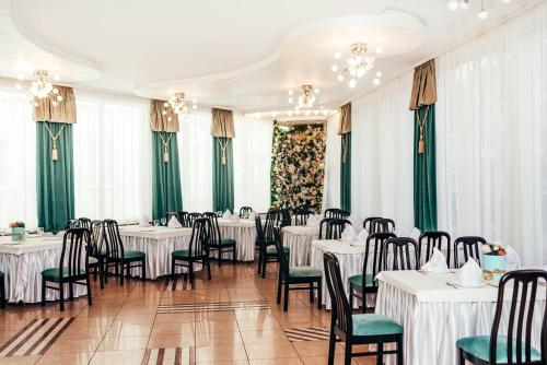 un restaurante con mesas y sillas blancas y cortinas verdes en Lyube, en Khmelʼnytsʼkyy