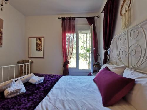 a bedroom with a white bed with purple sheets and a window at Apartamentos Alma y Montaña in Cómpeta