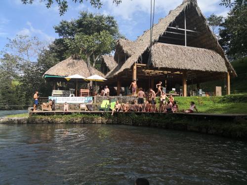 a group of people sitting outside of a hut next to a river at El Retiro Lanquin in Lanquín