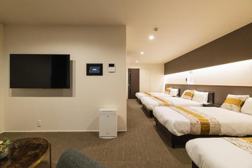 uma fila de camas num quarto de hotel com uma televisão de ecrã plano em GRAND BASE Nagasaki City em Nagasaki