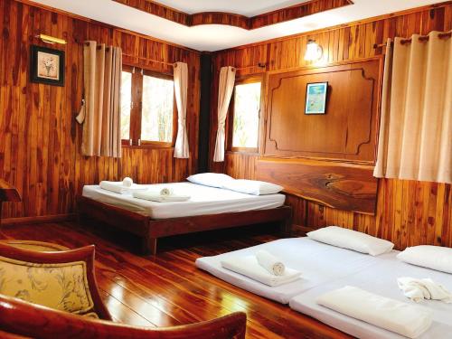 two beds in a room with wooden walls at คุ้งน้ำ รีสอร์ท นครนายก in Ban Khao Kariang (1)
