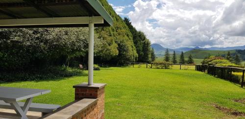 a picnic table in a field of grass with mountains at Pennygum Country Cottages in Underberg
